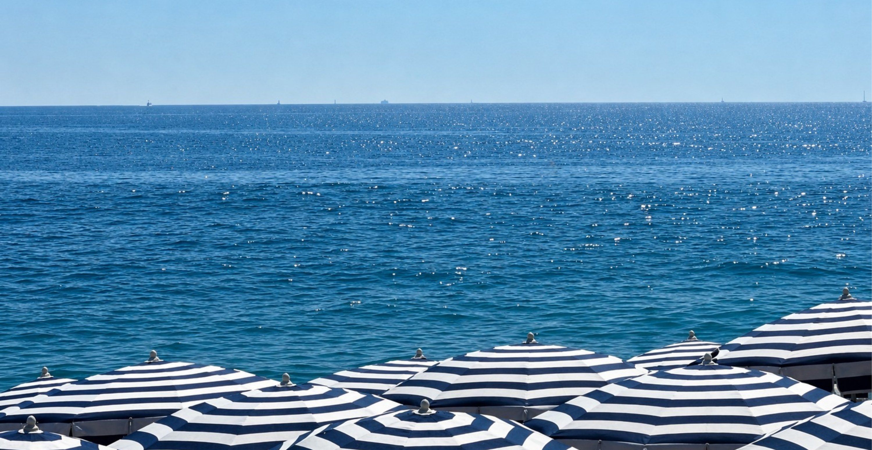Navy and white striped parasols along the shoreline of a beach club in Fethiye, with open sea behind