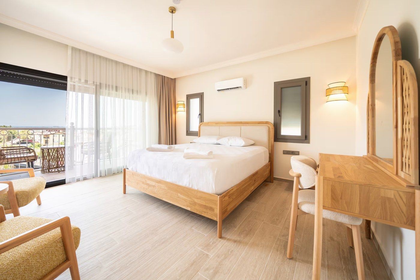 A double bed in pale oak beside balcony doors, with a round rattan mirror over the dressing table