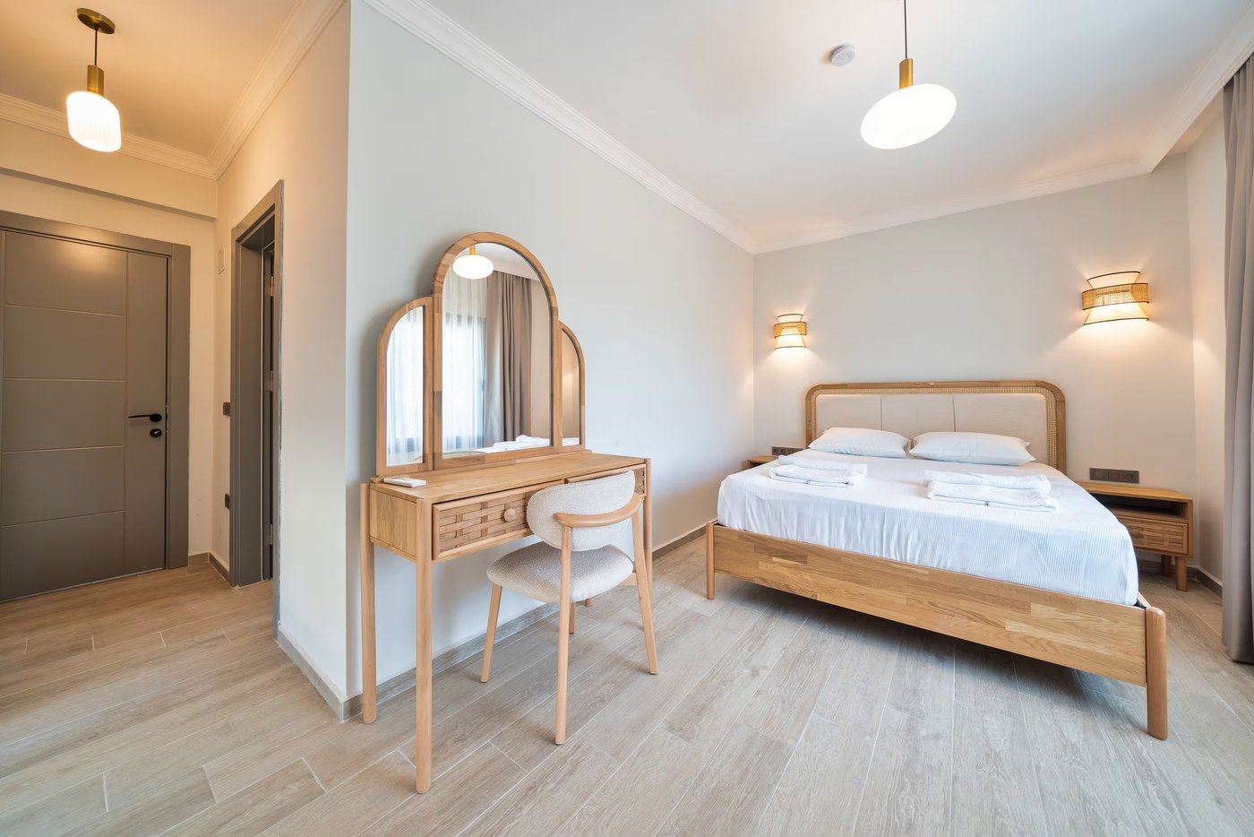 A double bed with an upholstered headboard, facing a dressing table under an arched mirror