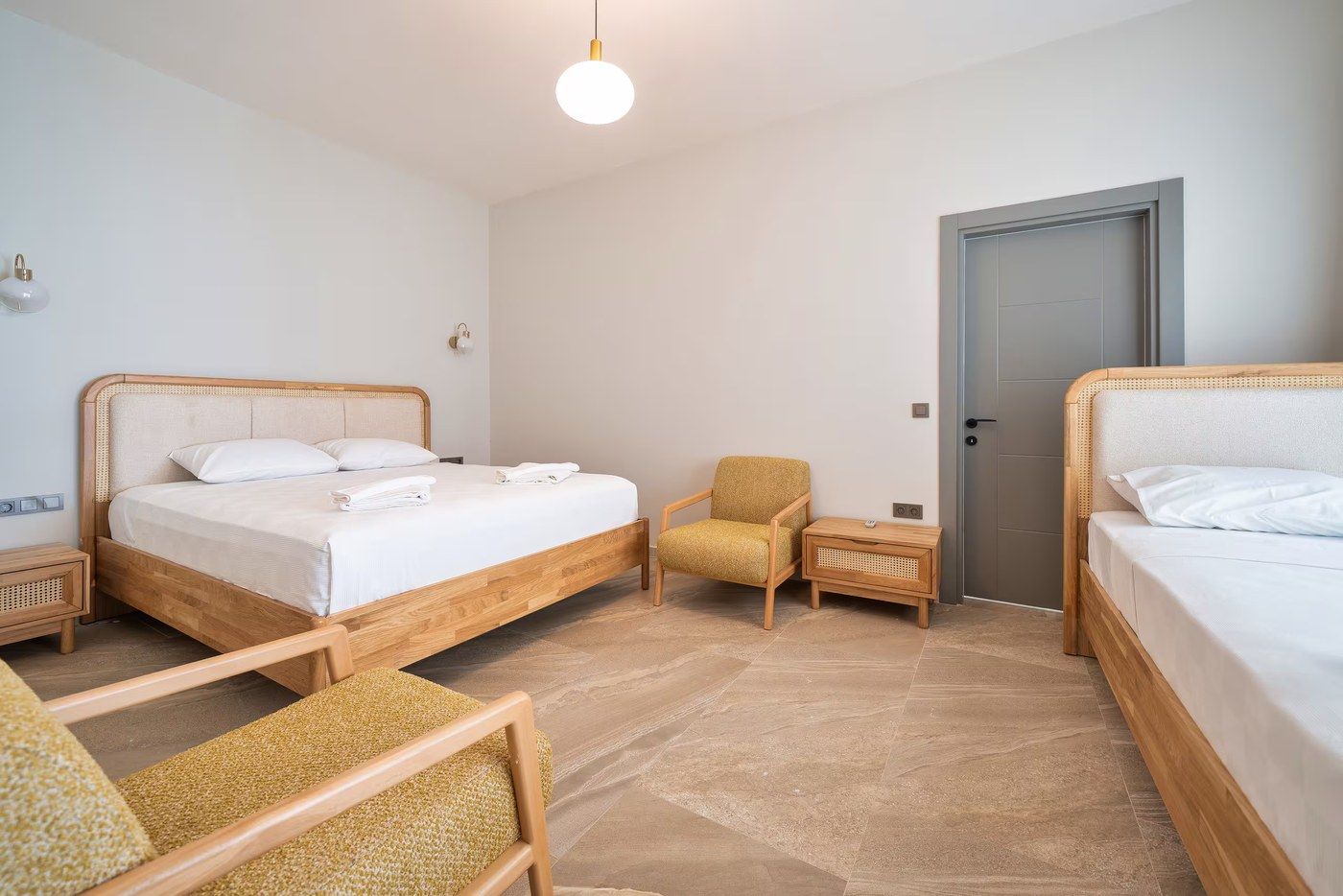 A double and a single bed under a sloped ceiling, with a mustard armchair between them